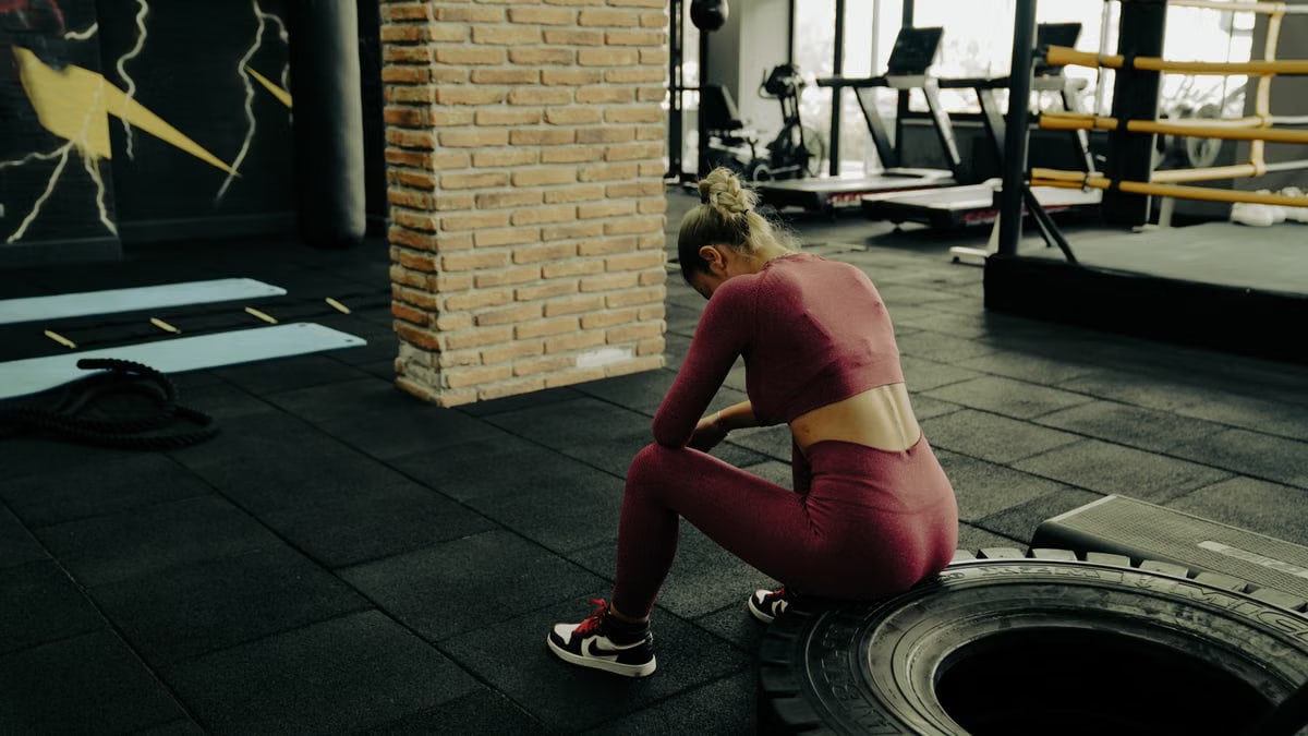 A woman in sportswear rests on a tire during gym training, showcasing fitness dedication.